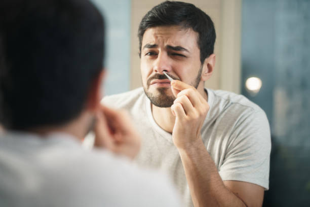 Handsome Man Trimming Nose Hair In Bathroom Young hispanic people and male beauty. Metrosexual man feeling pain when trimming nose hair with tweezers animal macho stock pictures, royalty-free photos & images