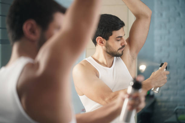 Man Using Spray Deodorant On Underarm For Bad Smell Young hispanic people and male beauty. Confident metrosexual man using spray deodorant on underarm skin, smiling and looking at mirror. mediterranean ethnicity stock pictures, royalty-free photos & images