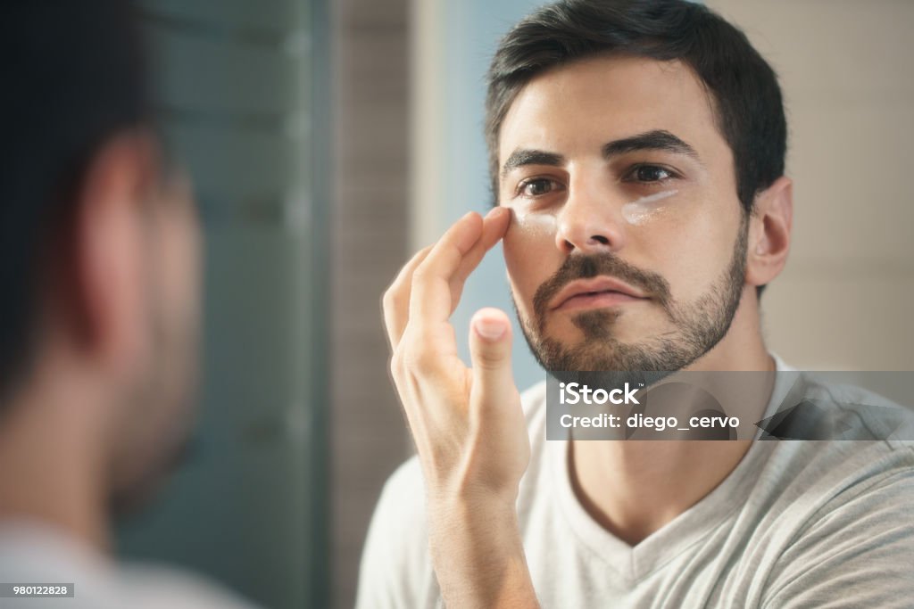 Young Man Applying Anti-aging Lotion fot Skin Care Young hispanic people and male beauty. Metrosexual man applying lotion for anti-aging treatment around eye Men Stock Photo