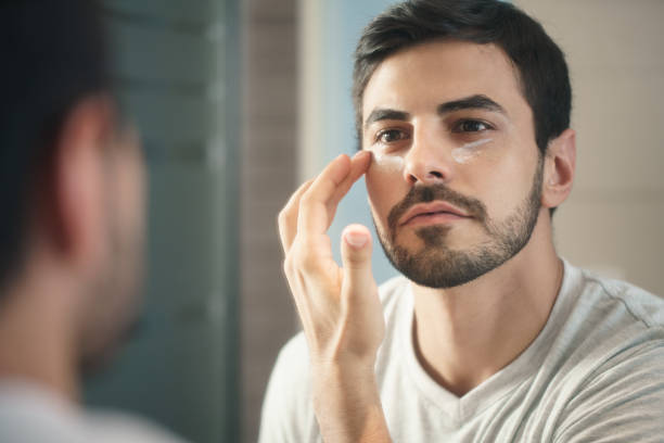 Young Man Applying Anti-aging Lotion fot Skin Care Young hispanic people and male beauty. Metrosexual man applying lotion for anti-aging treatment around eye only men stock pictures, royalty-free photos & images