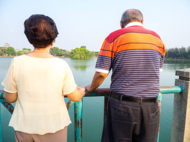 幸せなロマンチックな上級アジア カップルは湖の前に橋の上に立っています。夫は彼の妻と立っています。シニア カップルし、お互いの世話の概念 - senior adult couple care spring ストックフォトと画像