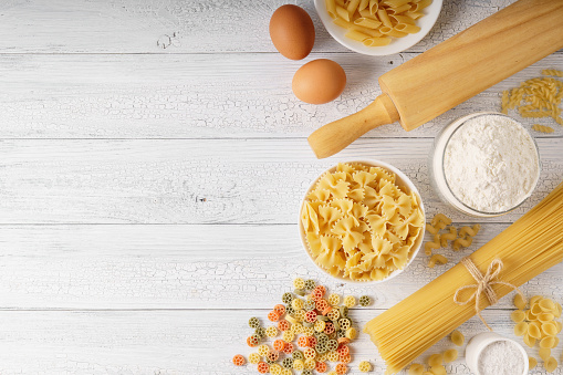 Dry mixed pasta, spaghetti and ingredients on a white rustic wooden background with a copy spaсe top view shot.