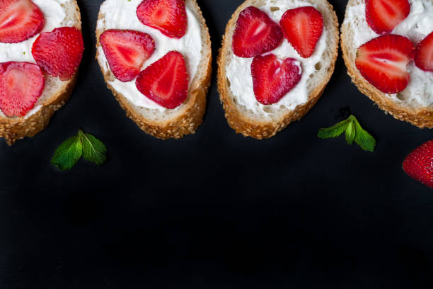 istock Toasts or bruschetta with strawberries on cream cheese on black background. 980174808