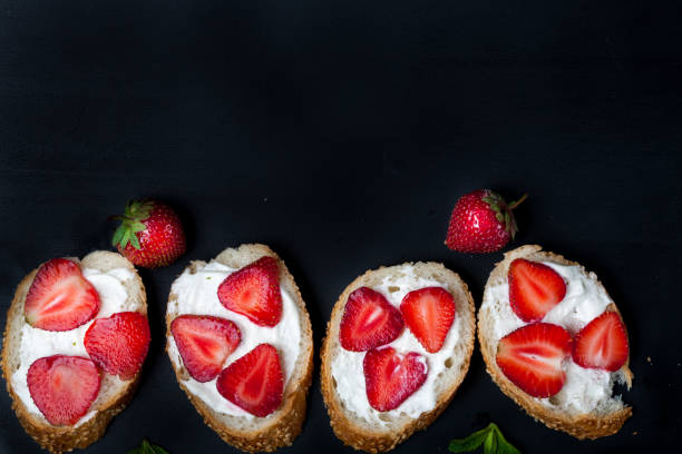 istock Toasts or bruschetta with strawberries on cream cheese on black background. 980174820