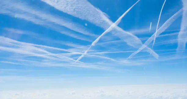 Multiple contrails cross paths through the sky above a layer of cloud over Germany.