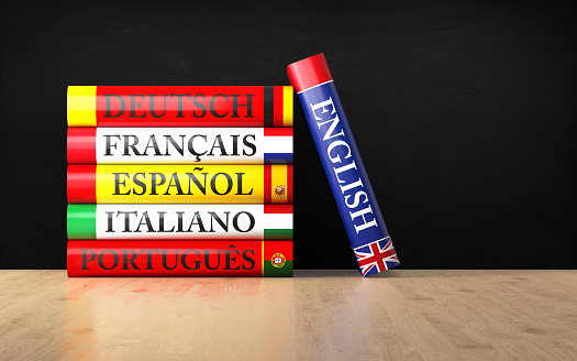 Stack of colorful dictionaries with a blackboard and a graduation cap in front of a black background. English, German, Portuguese, Spanish, French and Italian dictionaries are sitting on top of each other. Isolated on white background. Horizontal composition with copy space.