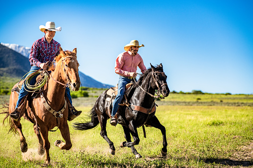 Two men galloping on horseback together in majestic Utah countryside.