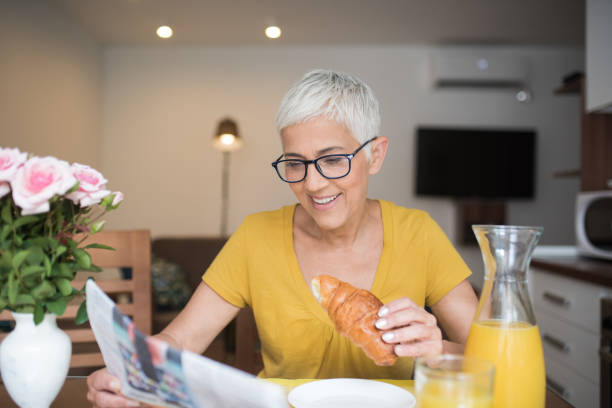 istock Smiling mature woman reading newspapers 980203274