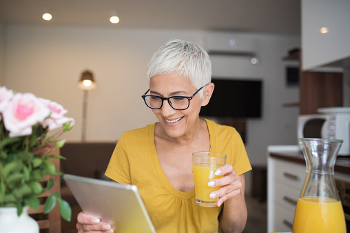 Smiling woman looking at digital tablet while drinking orange juice