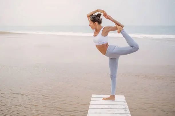 Photo of Caucasian woman practicing yoga at seashore of tropic ocean