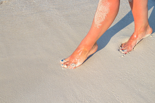 Crispy tanned women legs on the beach with sandy soles on the sandy beach