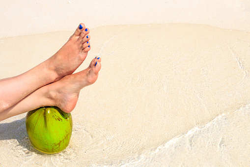 Woman feet and coconut on the sandy beach with crystal clear water