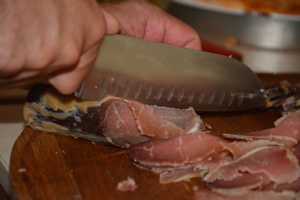 istock Butcher cutting pork meat on kitchen. Chef cutting beef meat on kitchen.Chef cutting fresh raw (smoked) meat on wooden board. Closeup of the hands of a butcher cutting slices of raw meat. 980263574