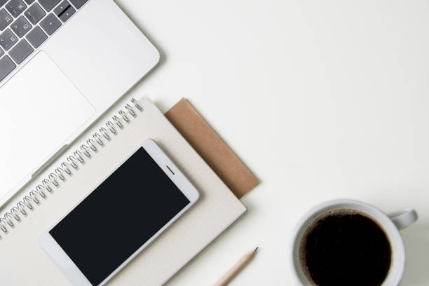 istock Top view of office workplace. White desk with copy space. Flat lay view on table with laptop, phone, notebooks, cup of coffee and pencil. Creative designer concept. 980272742