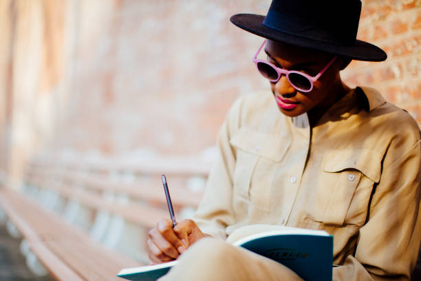 Female writing outside Portrait of a young woman writing into her notebook with pencil, under the shade of a tree in a public park poet stock pictures, royalty-free photos & images