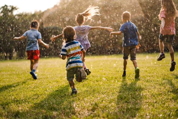 istock Back view kids running from a rain in park 980300678