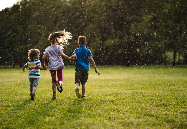istock three kids holding hands and running from a rain 980308082