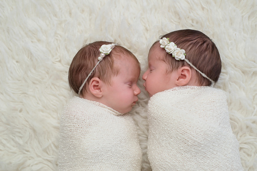 Profile headshot of two fraternal twin newborn baby girls sleeping and swaddled in white.