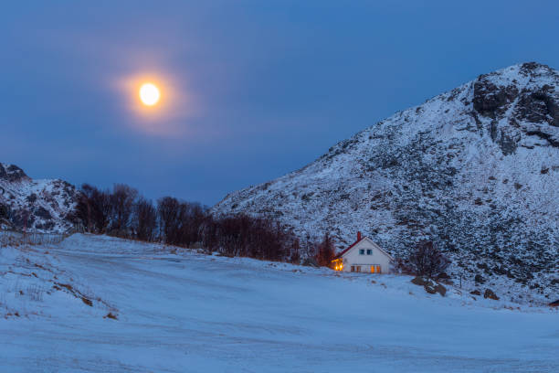 A house on a snowy mountain under moonlight on a winter evening at Vik, Lofoten, Nordland, Norway