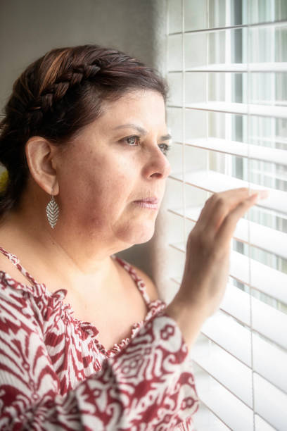 istock Smiling mature woman looking through a window 980386560