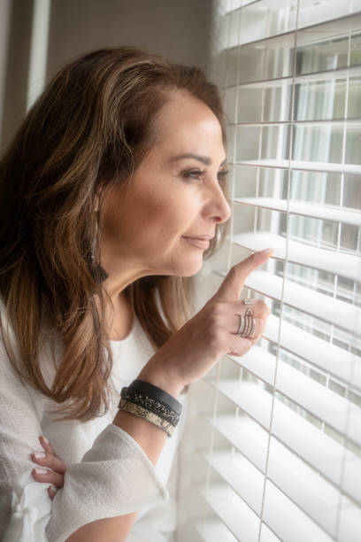 istock Smiling mature woman looking through a window 980386606
