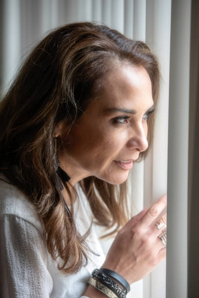 istock Smiling mature woman looking through a window 980387028