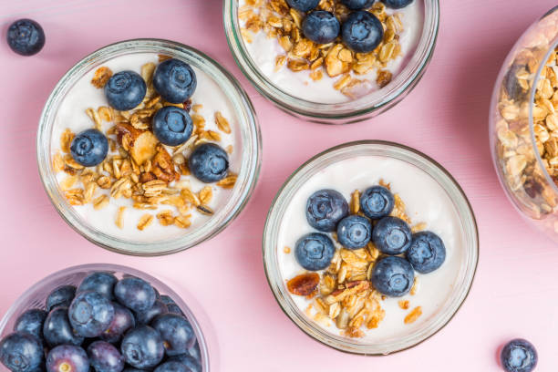 Yogurt with Homemade Granola and Blueberries Breakfast from Fresh Natural Yogurt with Homemade Granola and Blueberries in Glass Jars on Light Pink Background parfait stock pictures, royalty-free photos & images