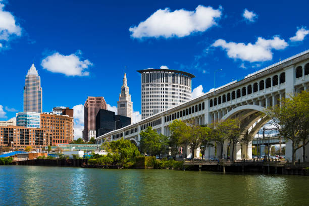 Cleveland Skyline With Bridge And Blue Sky With Puffy Clouds Downtown Cleveland skyline with the Detroit Superior Bridge and Cuyahoga River in the foreground, and a deep blue sky with puffy cumulus clouds in the background. detroit michigan stock pictures, royalty-free photos & images