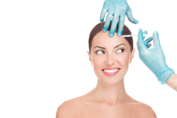 Happy woman receiving hyaluronic acid injection in her forehead stock photo
