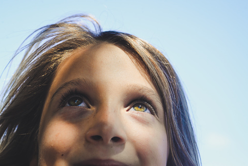 Sweet little girl in a outdoor shadowy portrait from the mouth up. Her eyes look up to the heavens. A blue, blue sky above her.