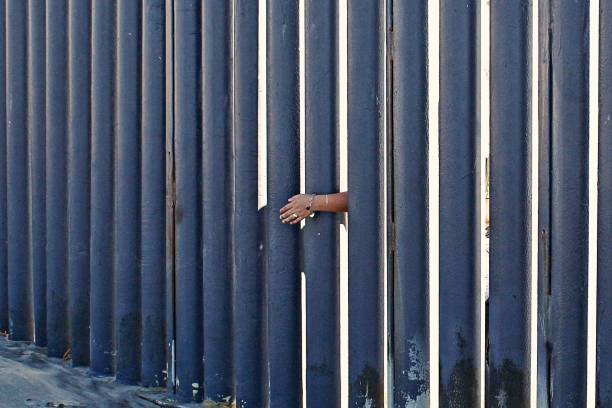 Border Hands Hands reach through the border wall of Mexico. international border barrier stock pictures, royalty-free photos & images