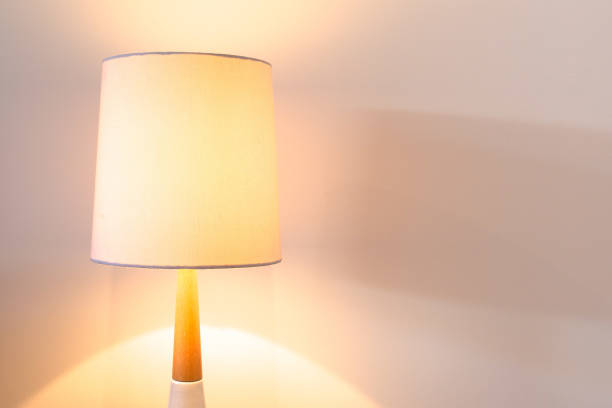 istock Bedroom lamp with white lampshade lit against white wall with copy space 980454562