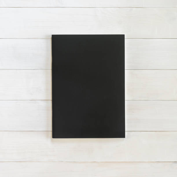 istock Book mockup blank black leather A4-size cover page template flat lay on white wood table from top view 980499266
