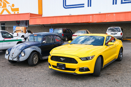 Palenque, Mexico - May 22, 2017: Yellow muscle car Ford Mustang and old car Volkswagen Beetle in the city street.