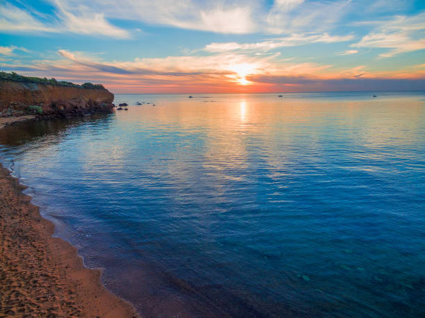 istock Beautiful sunset - sun touching tranquil ocean water near rugged coastline cliffs 980526990
