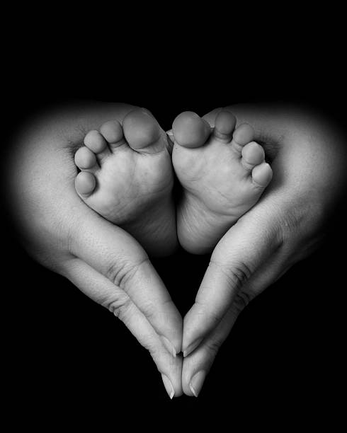 A baby's feet supported by mom's hands in the shape of a heart.