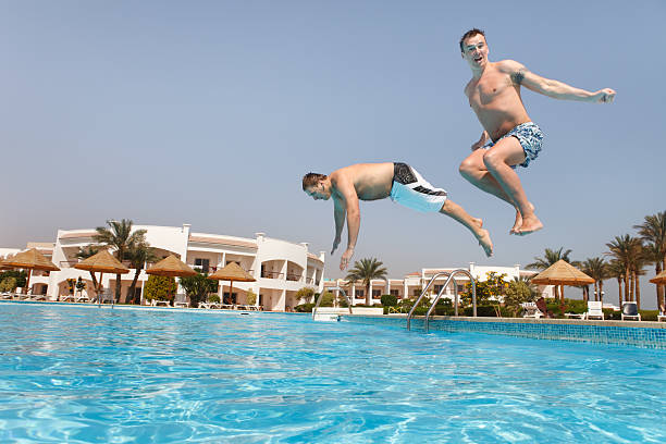 Two men jumping in swimming pool stock photo