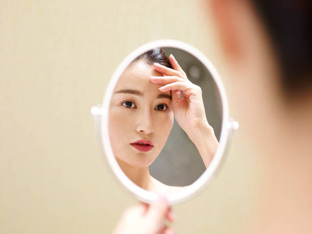 istock young asian woman looking at self in mirror 980585328