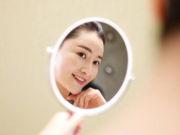 istock young asian woman looking at self in mirror 980585348