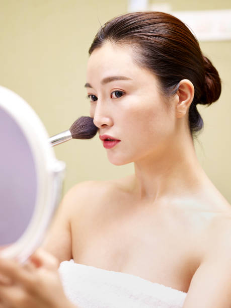 istock young asian woman looking at mirror while applying make-up 980585408