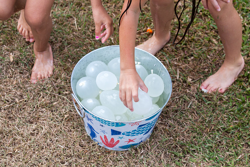 Kids grabbing water balloons from bucket on a hot summer day for a water fight in the garden.