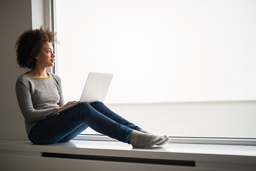 Young black woman using computer by the window and day dreaming. Copy space.