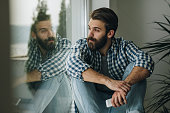 Thoughtful man relaxing on window sill at home.