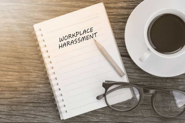 Workplace harassment concept on notebook with glasses, pencil and coffee cup on wooden table. Business concept.