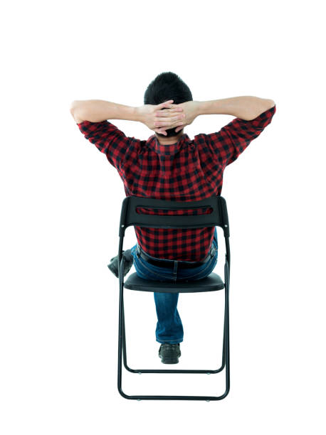 Man sitting on chair with hands behind head.
