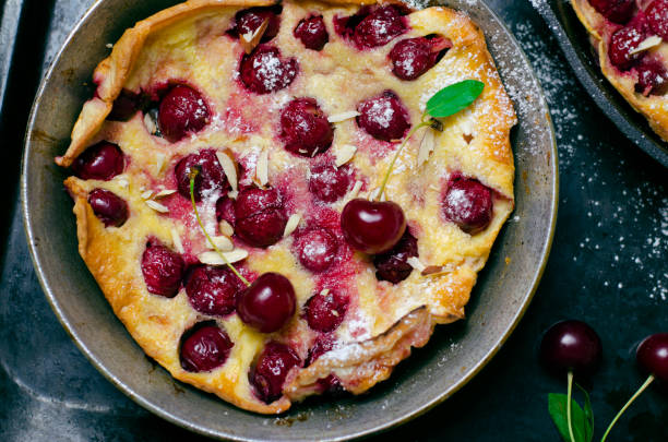 kirsche niederländische baby, blätterteig deutsche pfannkuchen auf vintage pfannen und dunklem hintergrund, hausgemachte sommer-dessert - clafoutis stock-fotos und bilder