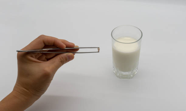 Handing holding milk teeth and little root with tweezer over a glass of milk isolated on white background. stock photo