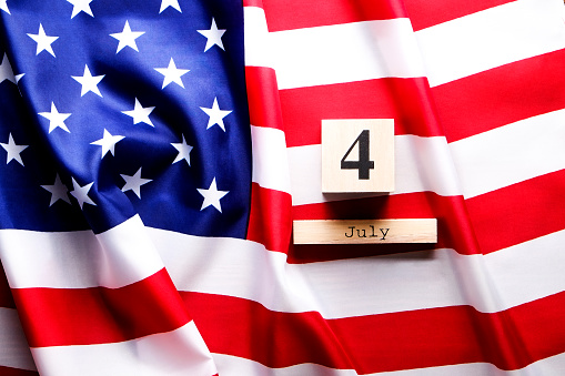 Ruffled American flag and wooden cube calendar with 4th of July, USA Independence Day date, copy space celebratory background. US patriotic festive composition, top view, close up.