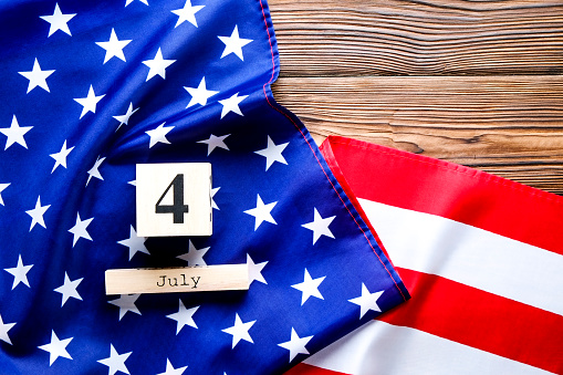 Ruffled American flag and wooden cube calendar with 4th of July, USA Independence Day date on brown wood vintage table, copy space background. US patriotic festive composition, top view, close up.