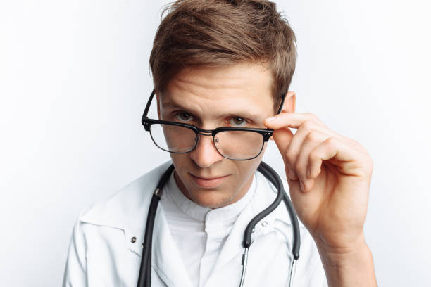 portrait d’un jeune médecin, sur un fond blanc, qui enlève ses lunettes et regarde la caméra, un stagiaire en studio, avec un stéthoscope au cou, pour la publicité, insertion de texte - trainee computer medical student student photos et images de collection